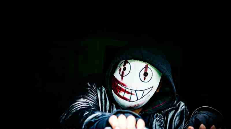 A mysterious figure wearing a creepy smiling mask in a dark setting, creating an eerie atmosphere., tags: und - pexel
