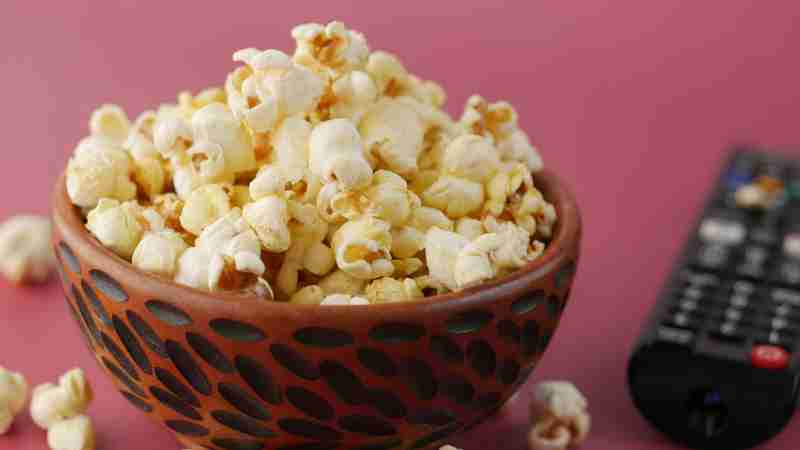 A vibrant close-up of popcorn in a decorative bowl beside a TV remote, ideal for snacks and entertainment themes., tags: kultklassiker - pexel